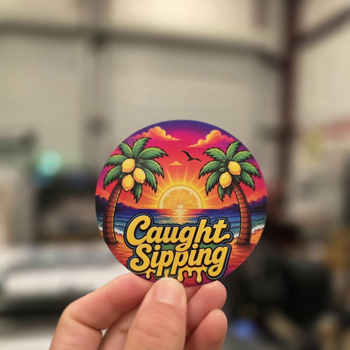 Hand holding a full color Caught Sipping circle sticker