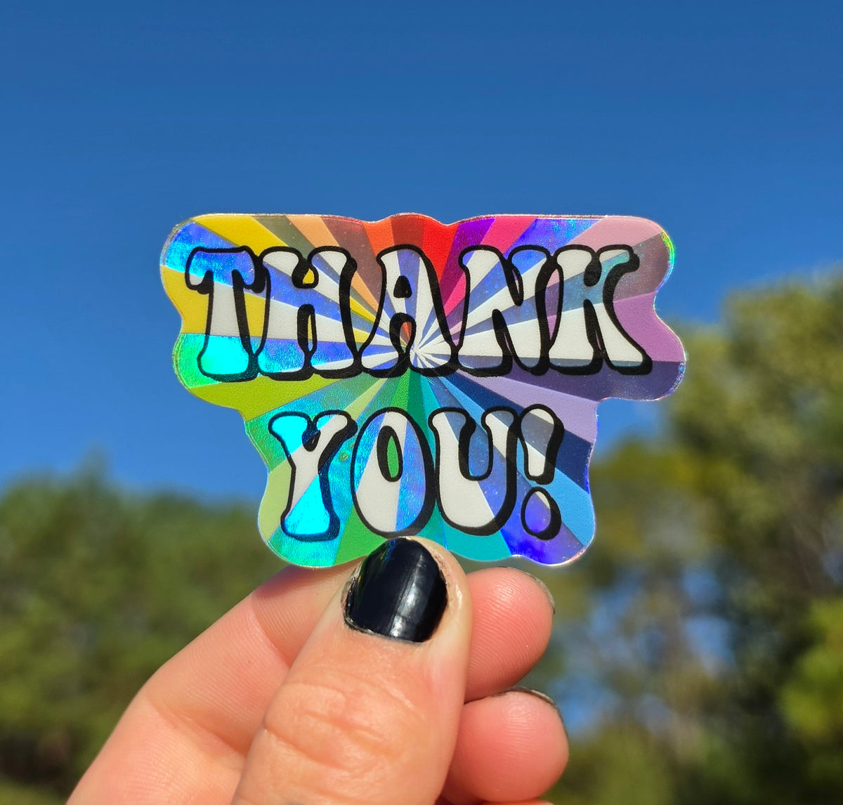 Holographic Thank You! sticker held up against a blue sky