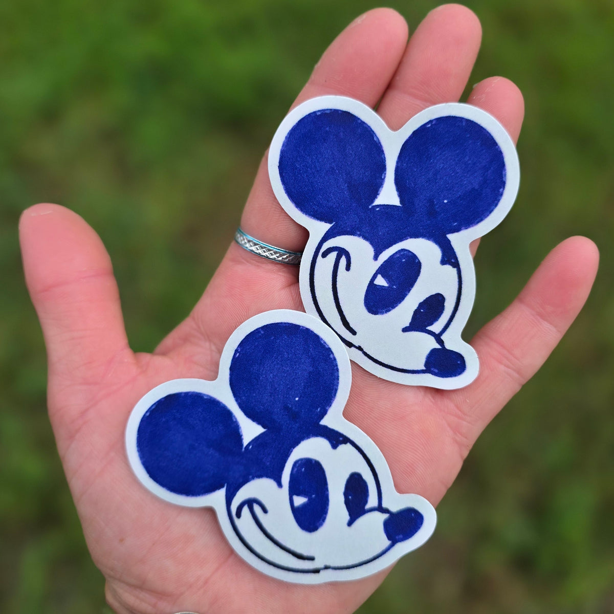Two blue and white cartoon mouse face die cut stickers held in an open hand